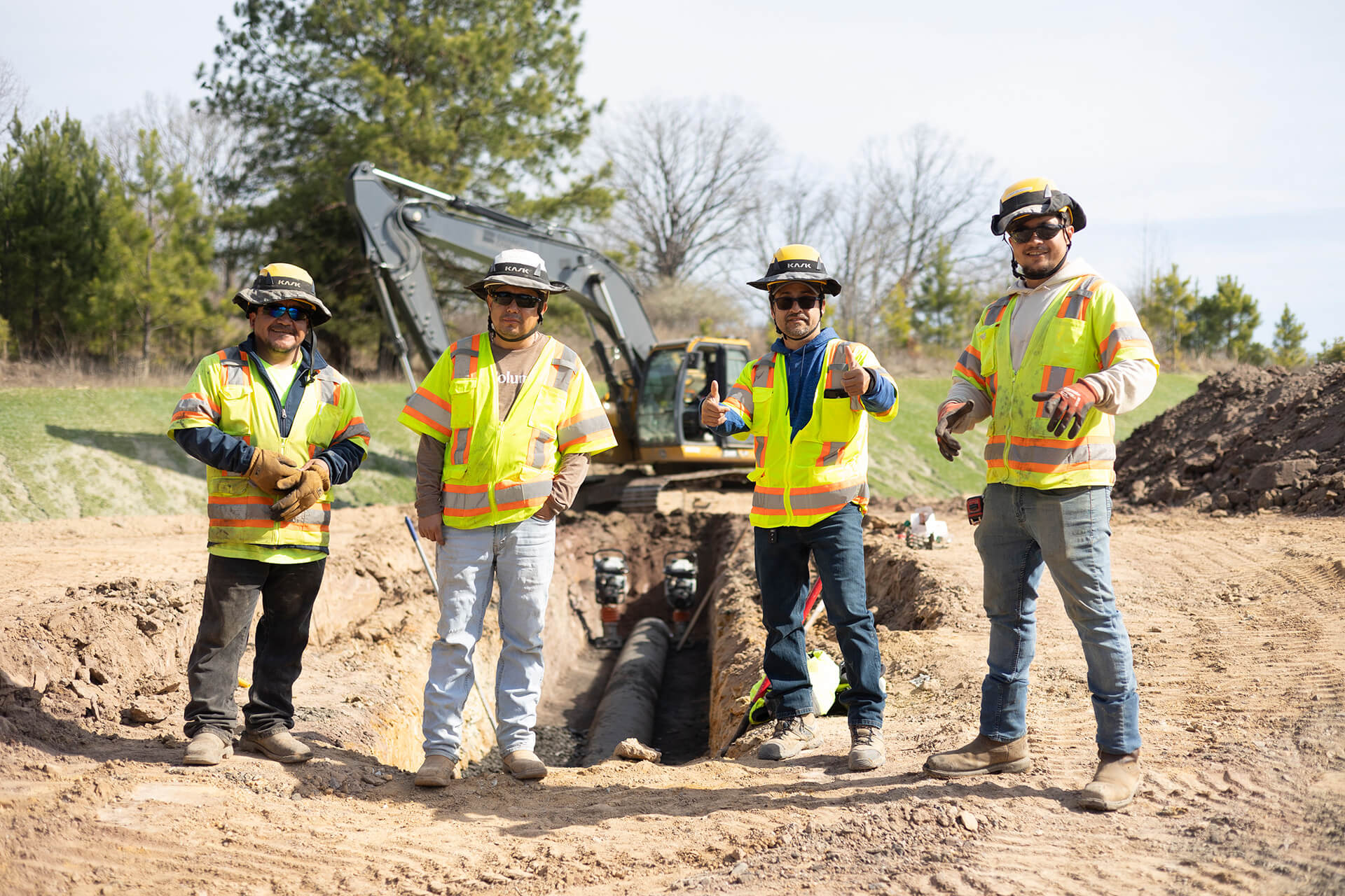 Branch Culture and People Four Men Standing on Jobsite with Excavator and Pipe