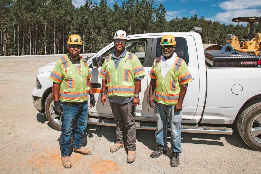 Group of Three Men Standing In Front of Truck on Jobsite
